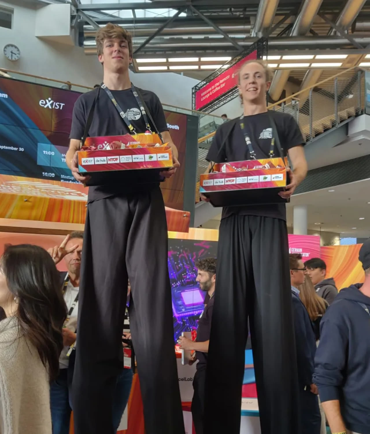 Zwei Stelzenläufer mit Bauchladen voller Give-aways auf einer Startup-Messe
